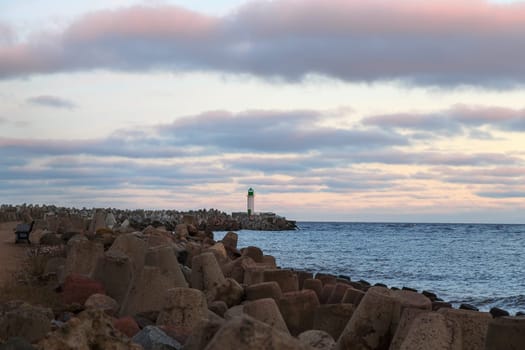 Seascape at sunrise with a lighthouse in the background, the sky with soft pink clouds