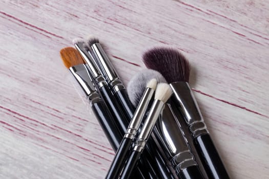 Closeup of a set of seven professional make up brushes on a light pink table background with copy space. Template for cosmetics product display montage or advertising text. Macro.