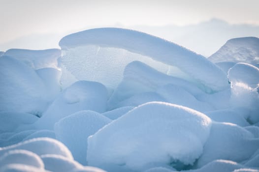 Transparent blue ice floes piled in ice hummocks against a blue sky on a sunny day. Unusual winter landscape of the frozen lake Baikal. Natural cold background. Siberia, Russia.