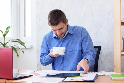 A man in a blue shirt sits at a table in the office with a napkin in his hand
