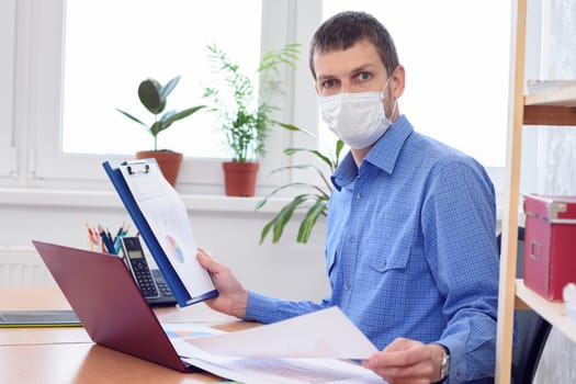 Office worker in medical mask examines data in documents with amazement