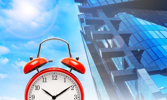 Red alarm clock on a modern townhouse and blue sky background. The concept illustration.