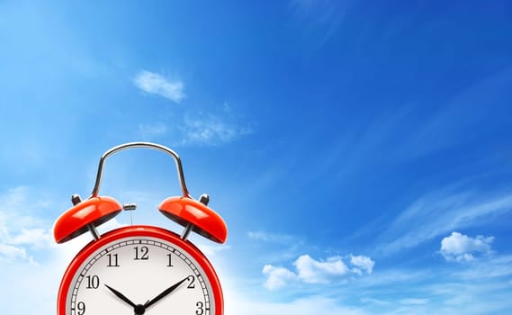 Analog red alarm clock on blue sky background with copy space..