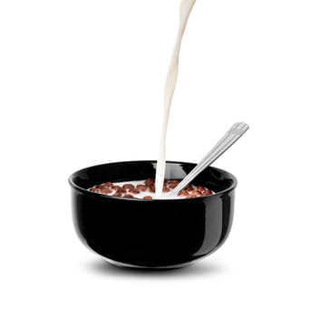 Pour a stream of milk on the chocolate flakes balls in a black bowl. Isolated on a white background. Close up with clipping path