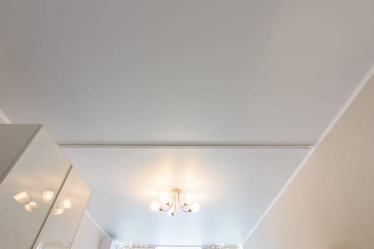 Classic white matte stretch ceiling with five lamp chandelier in the center