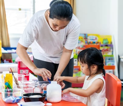 Asian girl kid playing toy and colorful paper for art lesson at living room in home as home schooling while city lockdown because of covid-19 pandemic across the world with quaratine mom as teacher.