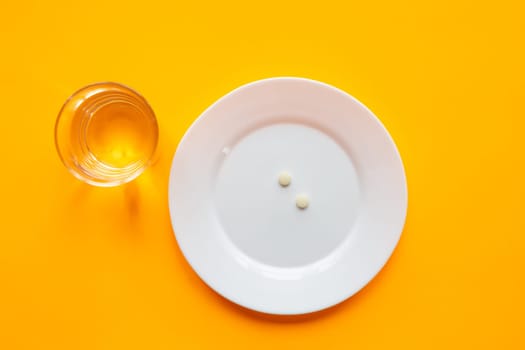 On the plate are two tablets, next is a glass of water