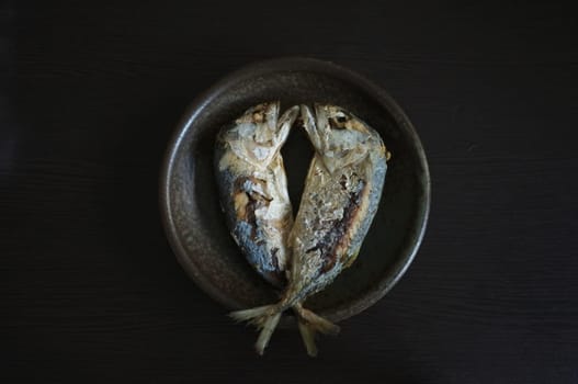 Fried two short bodied mackerel fishes on black background. Popular fish menu in Thailand.
