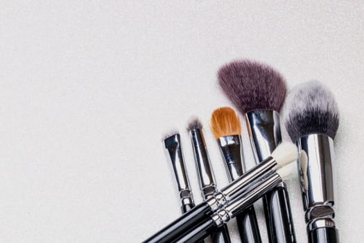 Closeup of a set of seven professional make up brushes on a bright glitter sparkle background with copy space. Template for cosmetics product display montage or advertising text. Macro.
