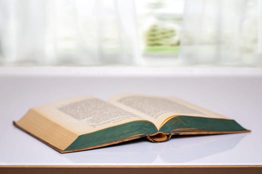 Close-up of an opened antique book on a bright table with blurred natural background. Education concept.