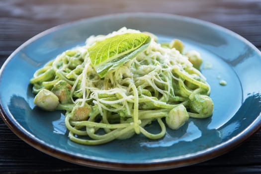 Green Pasta with scallop and sauce on blue plate