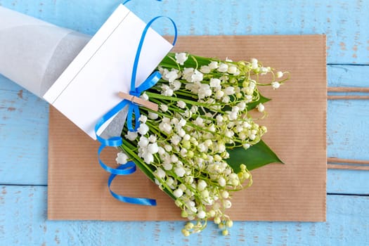 A bouquet of lilies of the valley in a paper bag on a wooden blue background with an attached business card