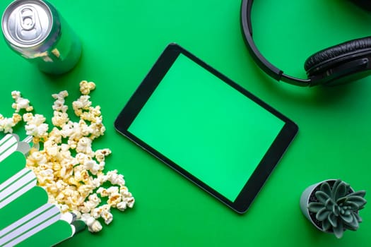 A tablet on a green background with popcorn and headphones
