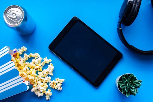 A tablet on a blue background with popcorn and headphones
