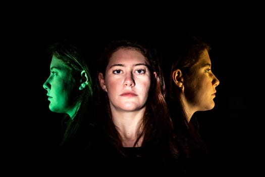 Face of a young woman frontal and multicolored in profile against a black background