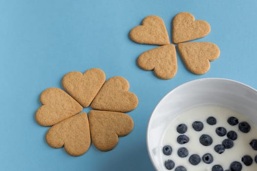 Breakfast. Close-up of heart shaped cookies like a flower petals. A bowl of yogurt with blueberries. Light blue background. Copy space.