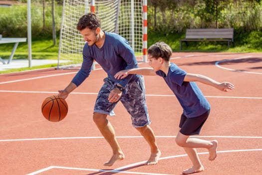 Father and son playing basketball barefoot on a playground