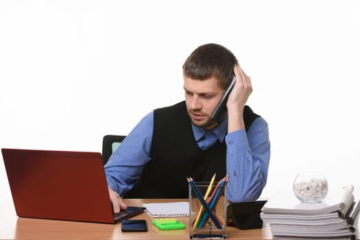 A tired employee negotiates on the phone looking into the screen of the laptop