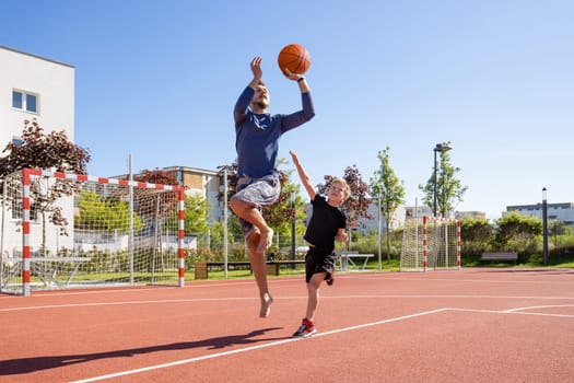 Dad and son playing basketball barefoot with the ball on a playground