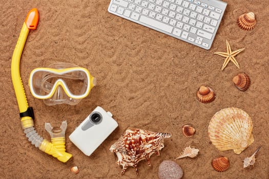 Equipment for snorkeling or diving, camera, computer keyboard, seashells on sand background. Top view with copy space. Summer holiday. Concept of sea vacation and travel. Travel agency. Internet shop