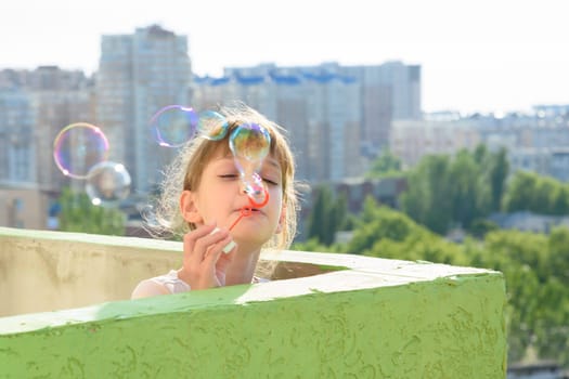 A child is having fun on the balcony of a multi-storey building blowing soap bubbles