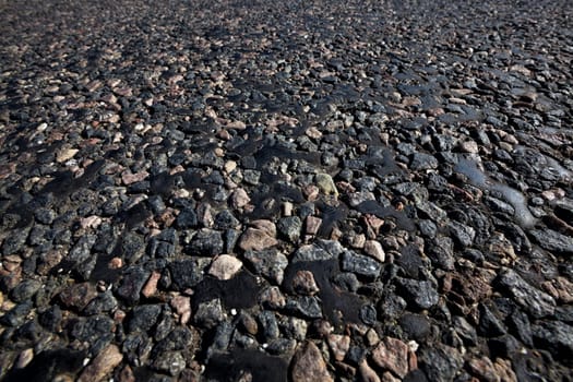 part of the paved road, close-up on the road drenched in black resin, which emerges through the stones and rubble