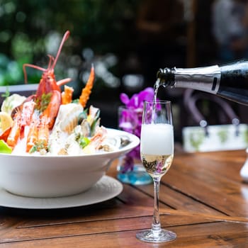 Waiter pouring white wine into wine glass and serving to customer in restaurant with big bowl seafood on ice in background. Restaurant gastronomy food and drink consumerism concept.