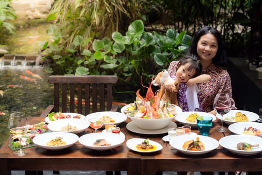 Portrait of mom and daughtersit at garden of restaurant of lobster shrimp steak beef lamb pasta spaghetti risotto rice sushi sashimi and wine using for buffet food drink background.