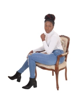 A young serious looking African American woman sitting in an old.armchair in jeans and white top, isolated for white background.