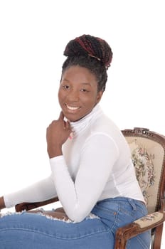 A smiling African woman sitting in a white top and jeans in an.old armchair, looking into the camera, isolated for white background.