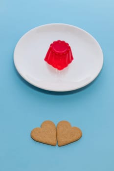 Close-up of a strawberry jelly dessert on a white plate. Two heart-shaped cookies.Light blue background