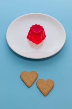 Close-up of a strawberry jelly dessert on a white plate. Two heart-shaped cookies.Light blue background