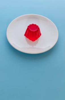 Close-up of a strawberry jelly dessert on a white plate with a light blue background. Copy space.