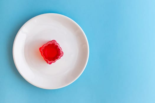 Close-up of a strawberry jelly dessert on a white plate with a light blue background. Copy space.