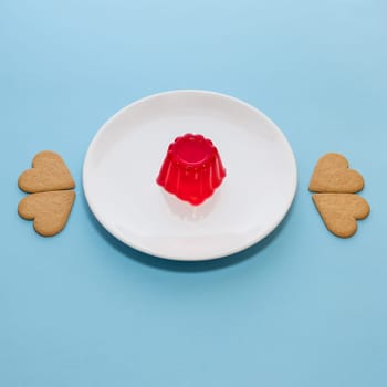 Close-up of a strawberry jelly dessert on a white plate. Heart-shaped cookies. Light blue background
