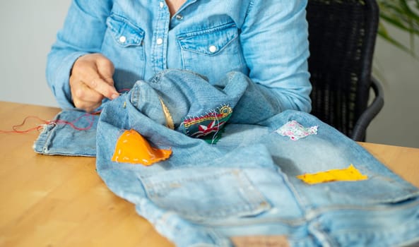 an elderly woman hands sewing on fabric jeans