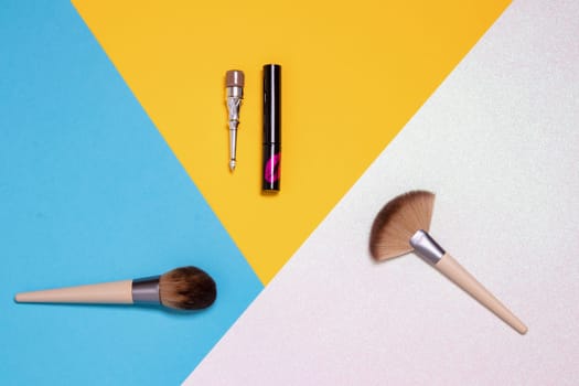 Decorative composition of colorful beauty and makeup products and tools such as brushes, eyebrow pencil, lipstick on a bright pink, yellow and blue background with copy space.. Advertising, design, cover and cosmetics background.