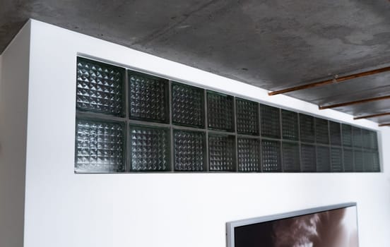 A cool-looking low cost glass blocks or glass bricks as a decorative addition in white wall under the ceiling to provide natural daylight, attractive appearance and energy efficiency in smart house