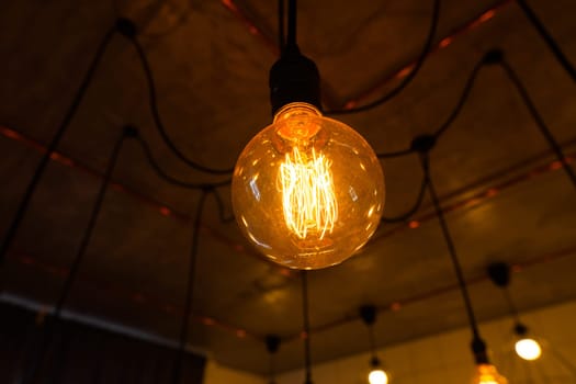 Close-up of big vintage incandescent lights bulb hanging in a dark room. Decorative edison light bulbs with straight wire. Dimmable, warm white, E27. Inefficient filament light bulbs waste electricity