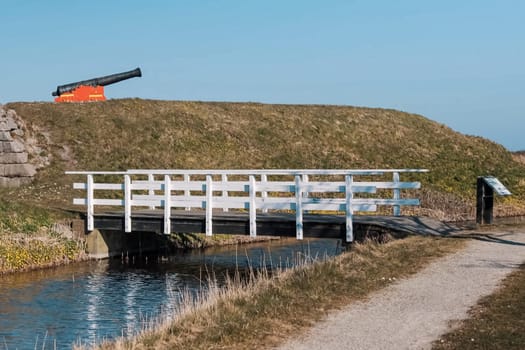 A wooden bridge over a small river. A gun on a hill. Open-air museum
