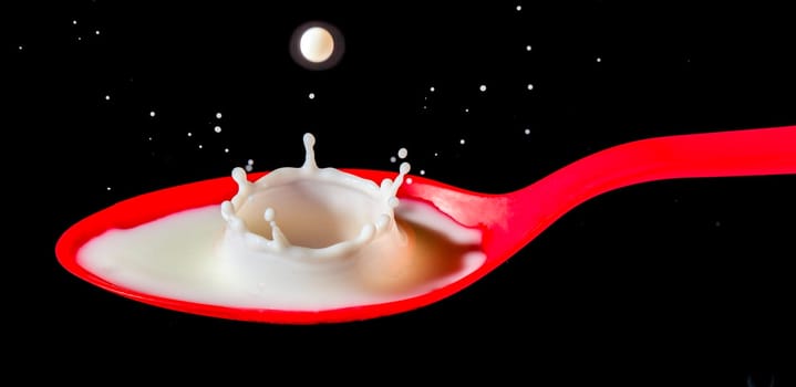 White milk splashing into red spoon