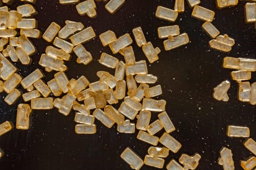 Macro of refined crystallised sugar with rectangular golden granules on a dark background
