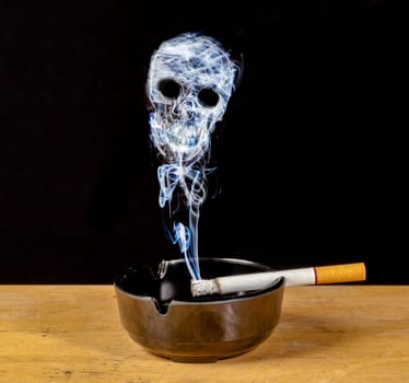 Burning cigarette in an ashtray with a skull formed of smoke , a warning of the hazards of smoking