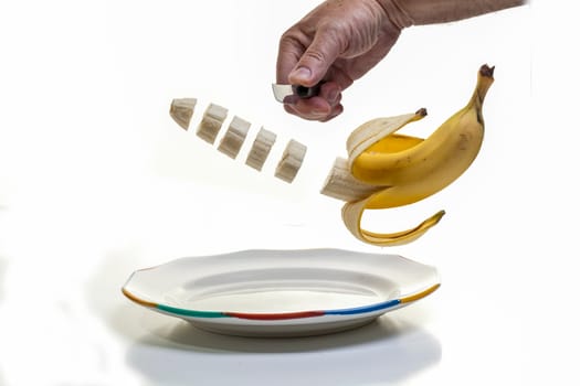Slicing up breakfast  - A human hand holding a knife and slicing a half peeled banana with the slices suspended midair over a plate