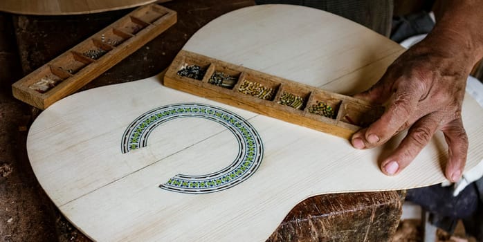 Man puts finishing touches on the inlay around a soundhole in a new instrument