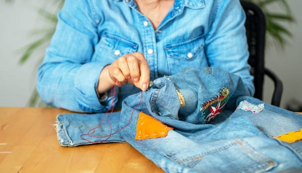 an elderly woman hands sewing on fabric jeans