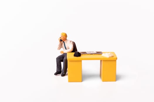 Miniature people businessman holding a telephone sitting behind his work desk. Macro shot of Tiny people business concept.