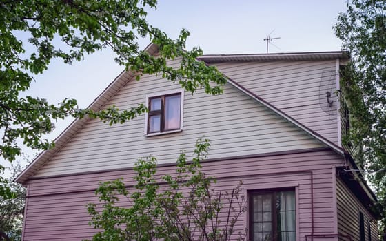 Low angle view of the top of a country house with an attic and a mezzanine. Simple residential cottage with siding paneling in the spring .garden. Russia. Selective focus.