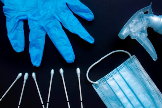A close up of medical items: throat swabs, gloves, medical face mask and spray disinfecting liquid spray on a black background.