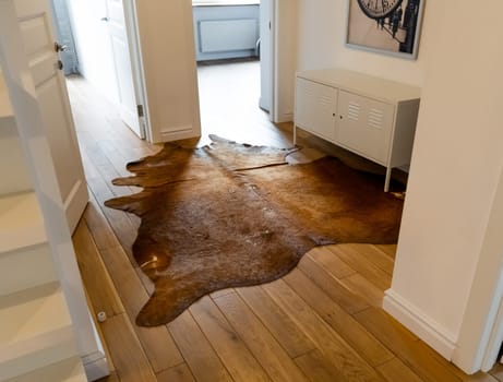 Reddish Brown Cowhide rug with silky coat on a wooden floor as luxuriously home decoration with rustic or western charm. A cow skin carpet in industrial-styled corridor as addition to modern interior